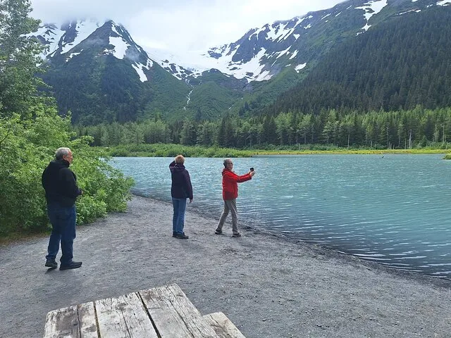Tourists standing on a gravel shore looking at a glacier lake