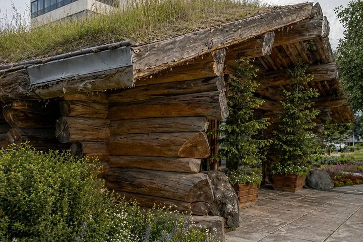 A wooden cabin structure with a sod roof and green plants